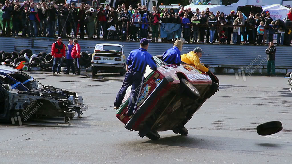 Stunt Performers Change Tire While Driving Car On Two Wheels Stock